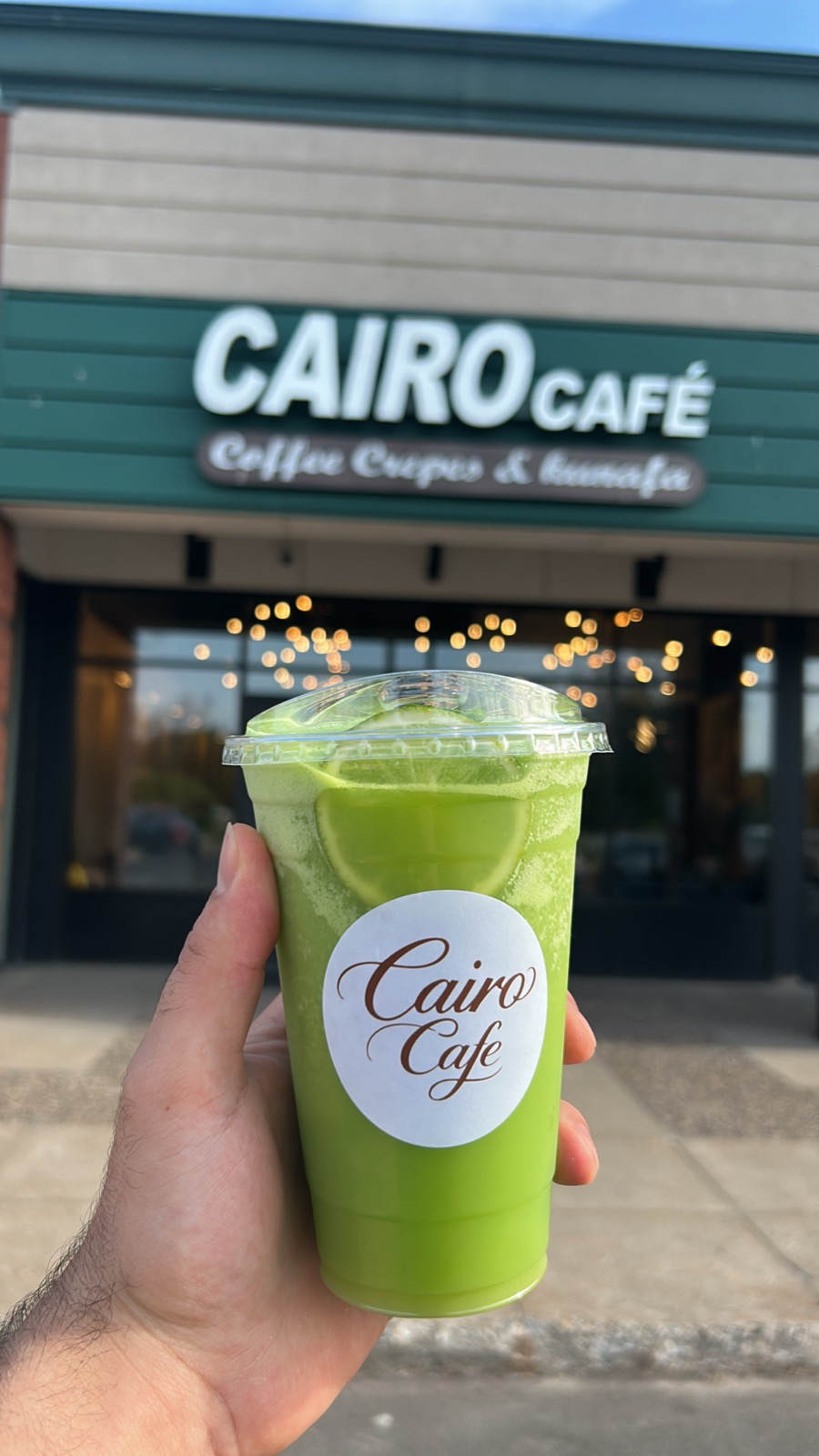 Iced matcha held in front of the Cairo Café storefront